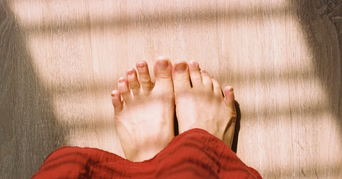 Top-down view of a pair of bare feet on a sunlit wooden floor, showing the spread of the forefoot.