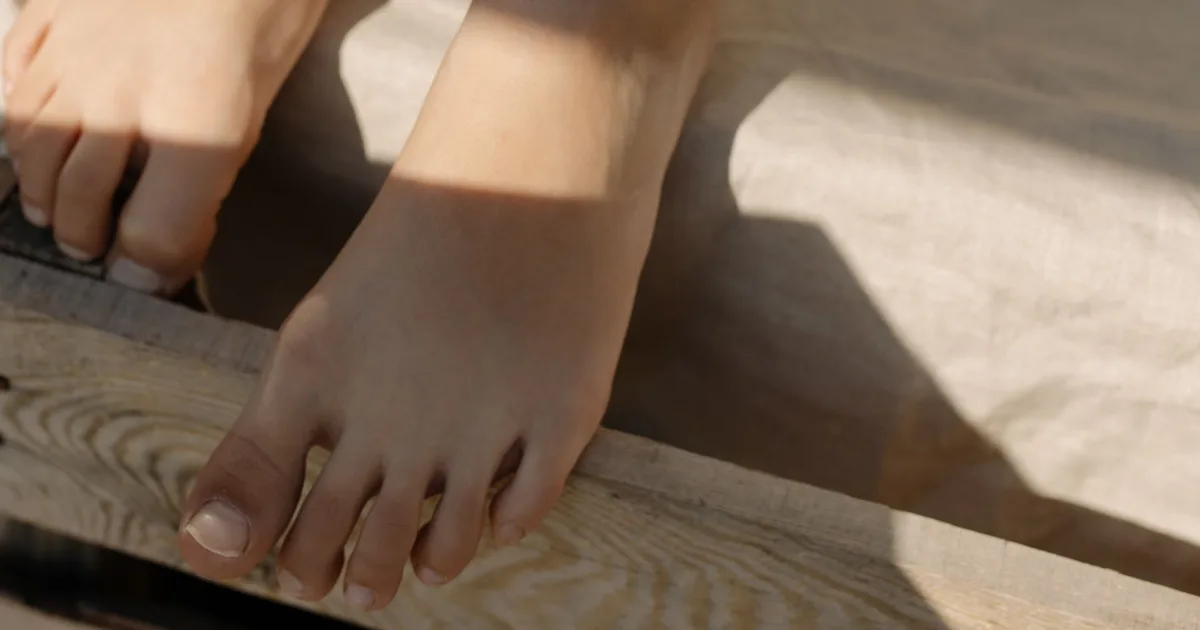Close-up of bare feet with the toes and toenails visible, resting on a sunlit wooden surface.