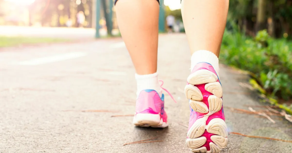Rear view of a woman walking along a paved path in cushioned walking shoes.