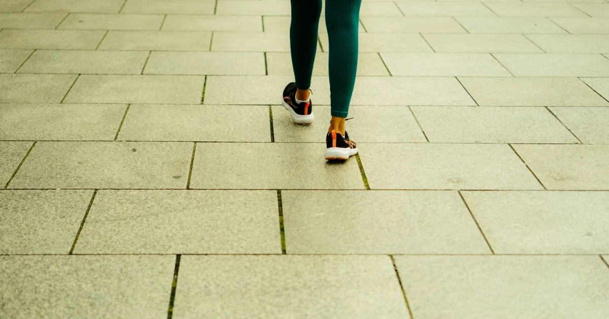 A person walking away from the camera along a stone-tiled city sidewalk.