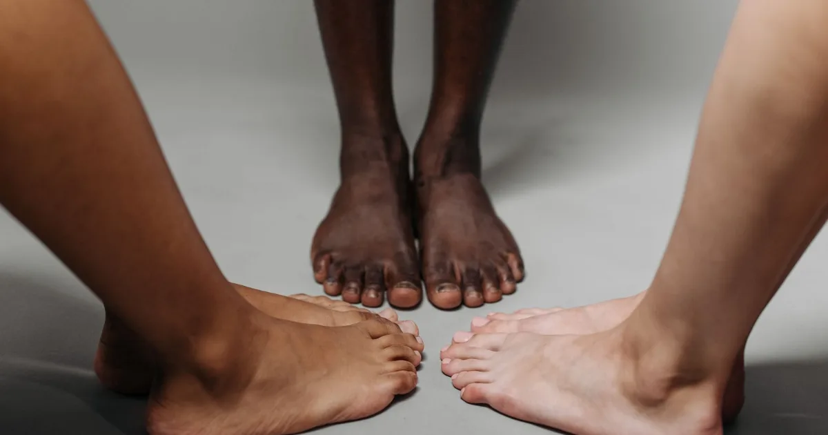 Three pairs of bare feet standing together on a neutral surface — best shoes for overpronation, Podiatrist Tested