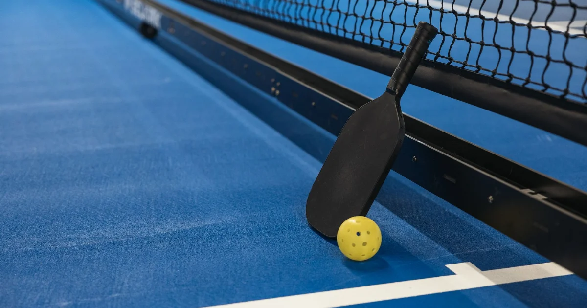 A pickleball paddle and ball on a blue court - best shoes for pickleball, Podiatrist Tested