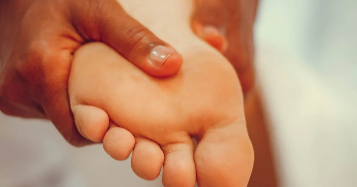 A hand pressing into the sole of a bare foot with the thumb, in the arch.