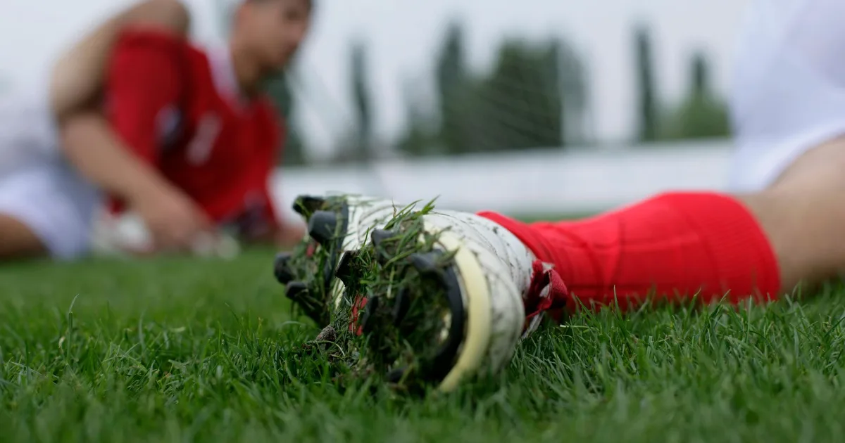 Low-angle view of a soccer cleat lying on grass with its stud plate packed with turf.
