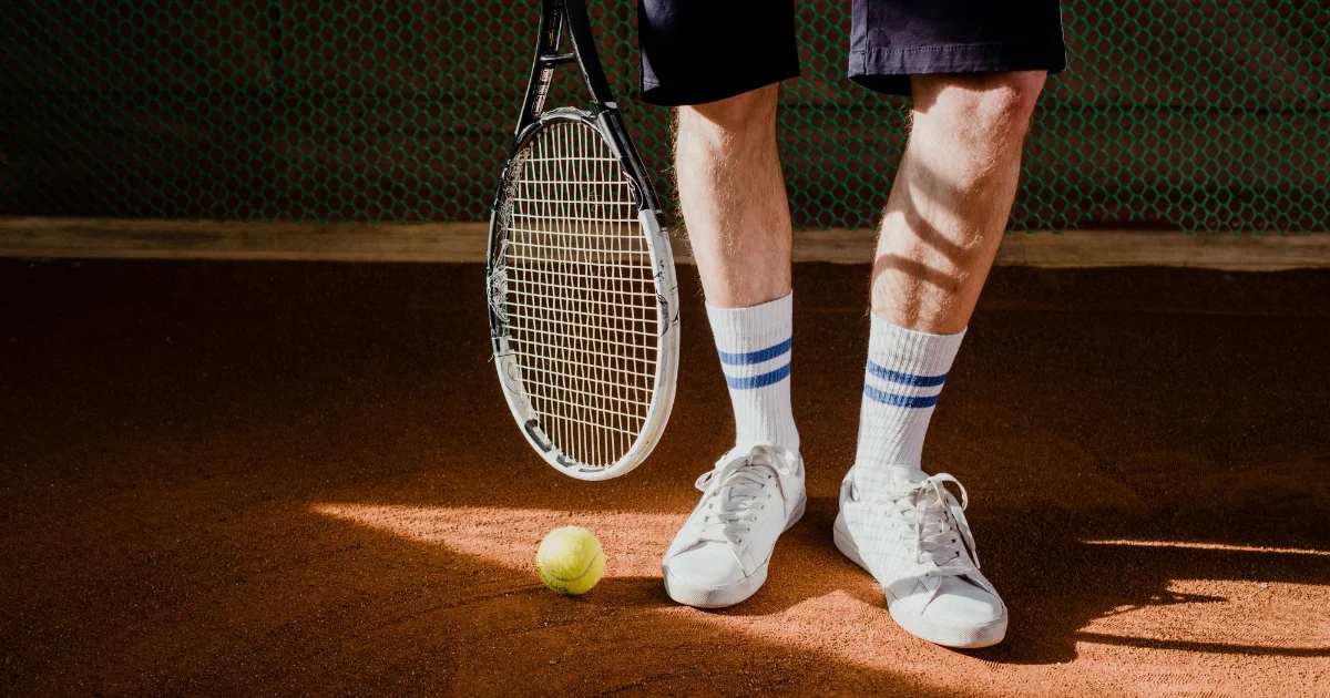 A player legs, racket and ball on a clay tennis court - best tennis shoes for plantar fasciitis, Podiatrist Tested